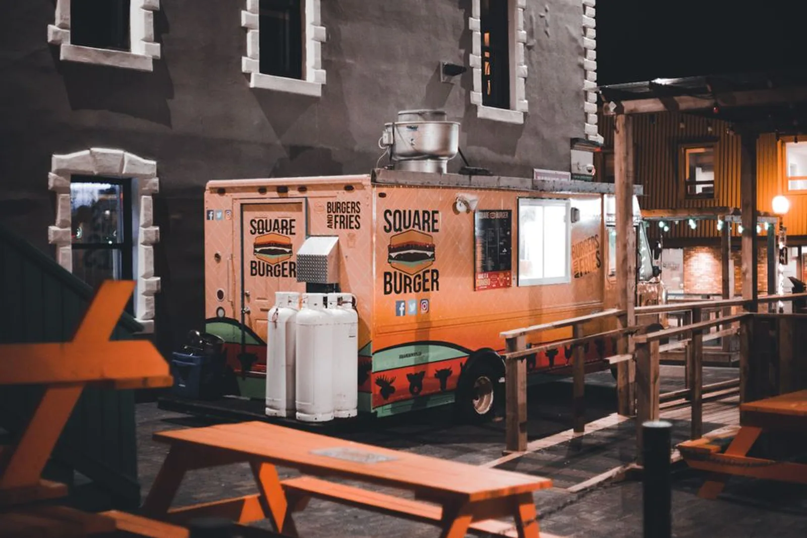 Food truck de hambúrguer iluminado à noite com mesas ao ar livre