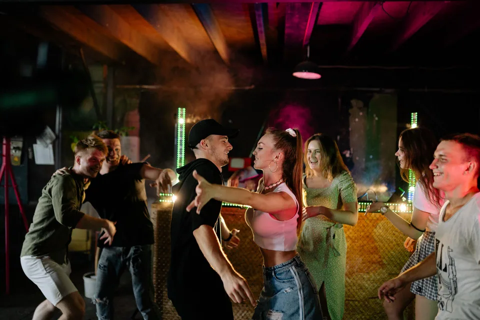 Grupo de jovens dançando animados em um bar com luzes coloridas