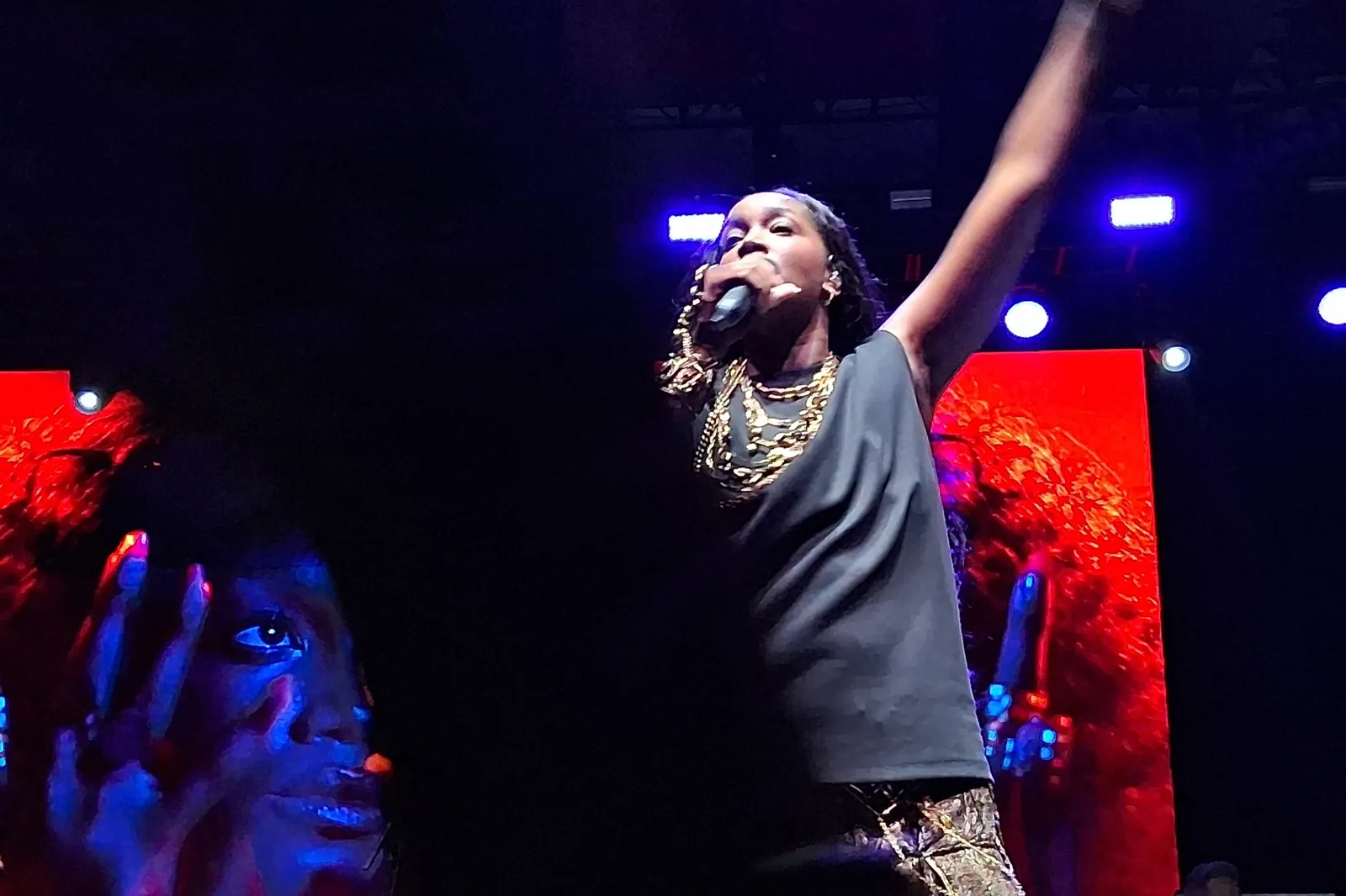 Iza canta de braço erguido e microfone na mão, de camiseta escura e correntes douradas, em show ao ar livre em Nova York em 2025