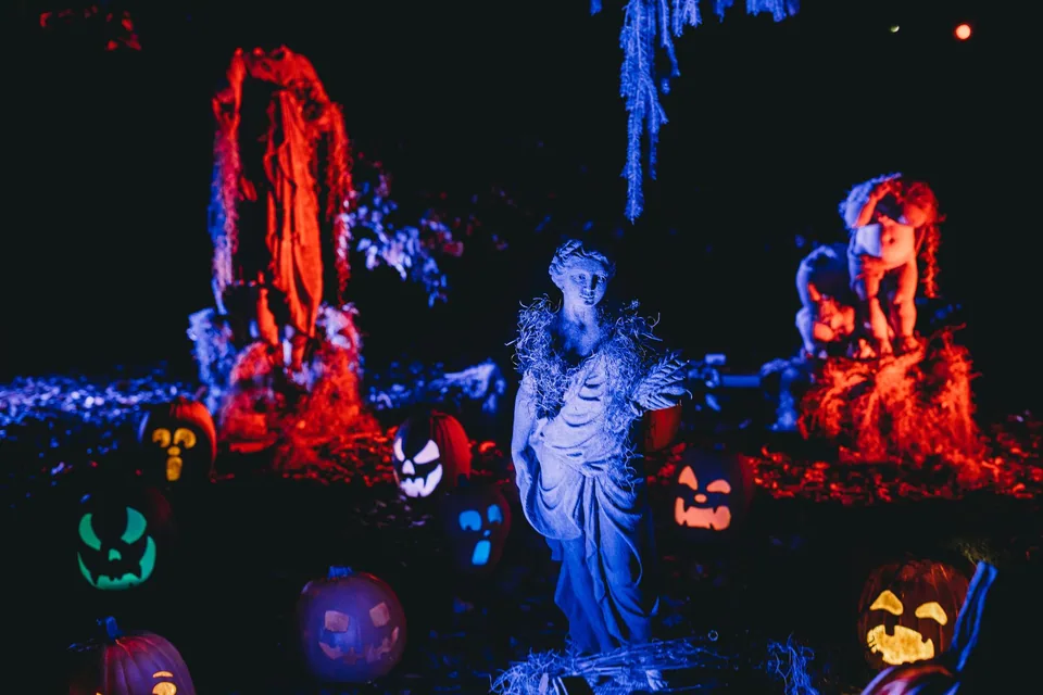 Abóboras esculpidas iluminadas em azul, vermelho e verde ao redor de uma estátua, em cenário de Halloween