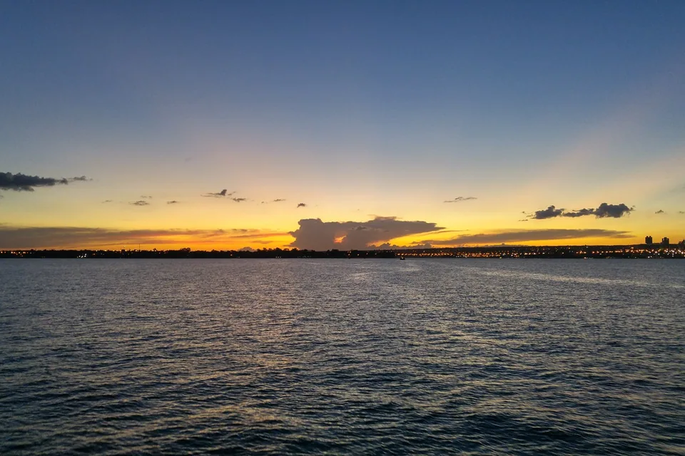 Lago Paranoá ao entardecer, com céu alaranjado e as luzes da cidade na margem