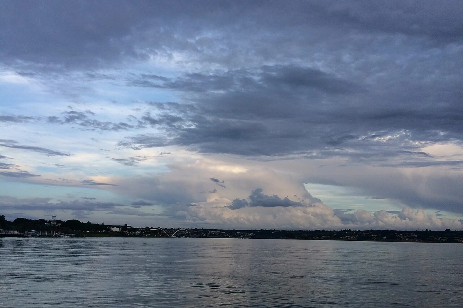 Lago Paranoá ao entardecer, com a Ponte JK ao fundo e céu carregado de nuvens