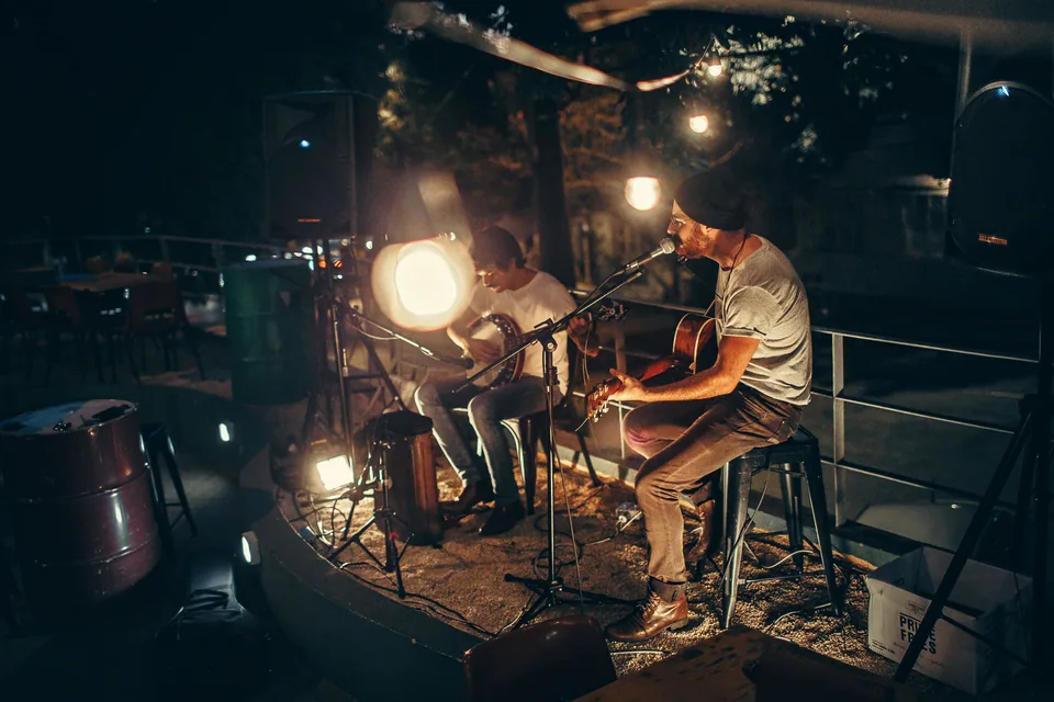 Dois músicos tocam violão ao ar livre à noite, foto ilustrativa