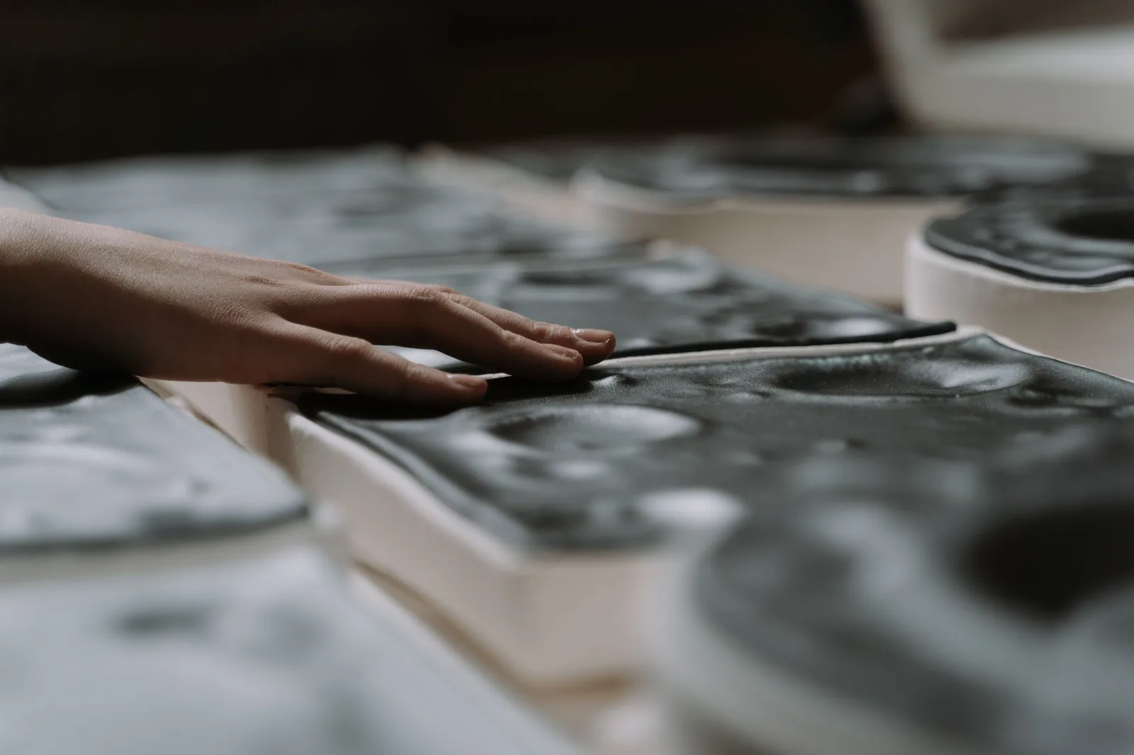 Mão toca a superfície de peças de cerâmica escura, em foto ilustrativa de arte tátil