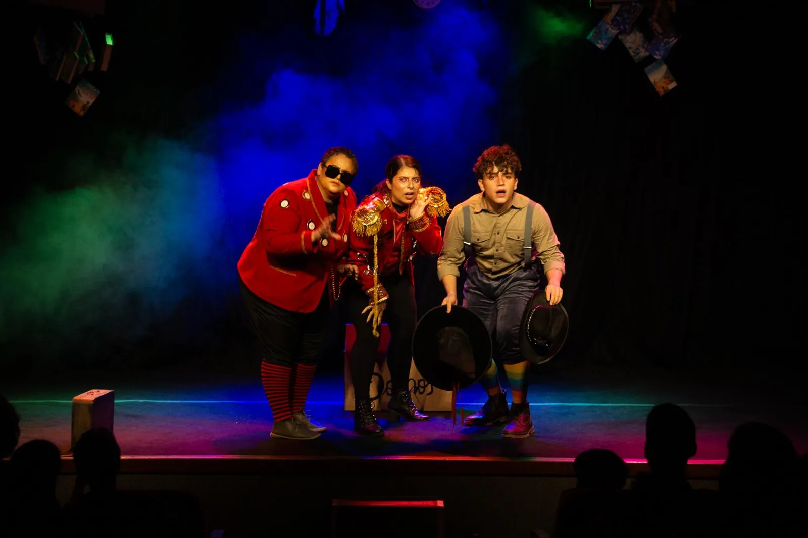 Atores em figurino vermelho e suspensório em cena do musical O Menino e o Tempo, com fumaça e luz azul