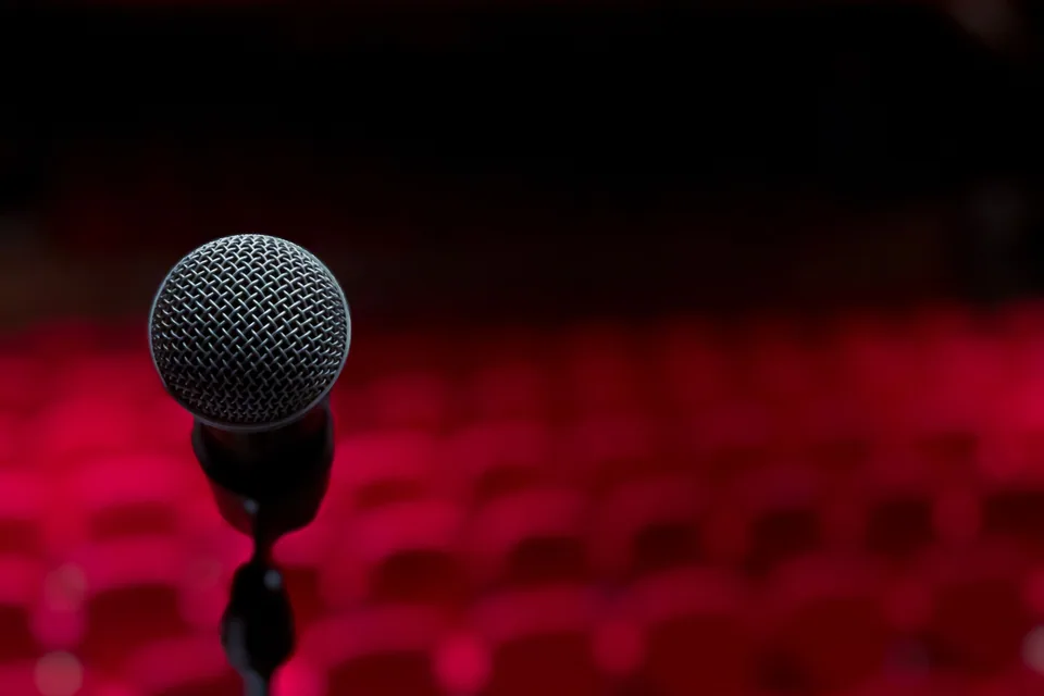 Microfone em primeiro plano com poltronas vermelhas de teatro desfocadas ao fundo