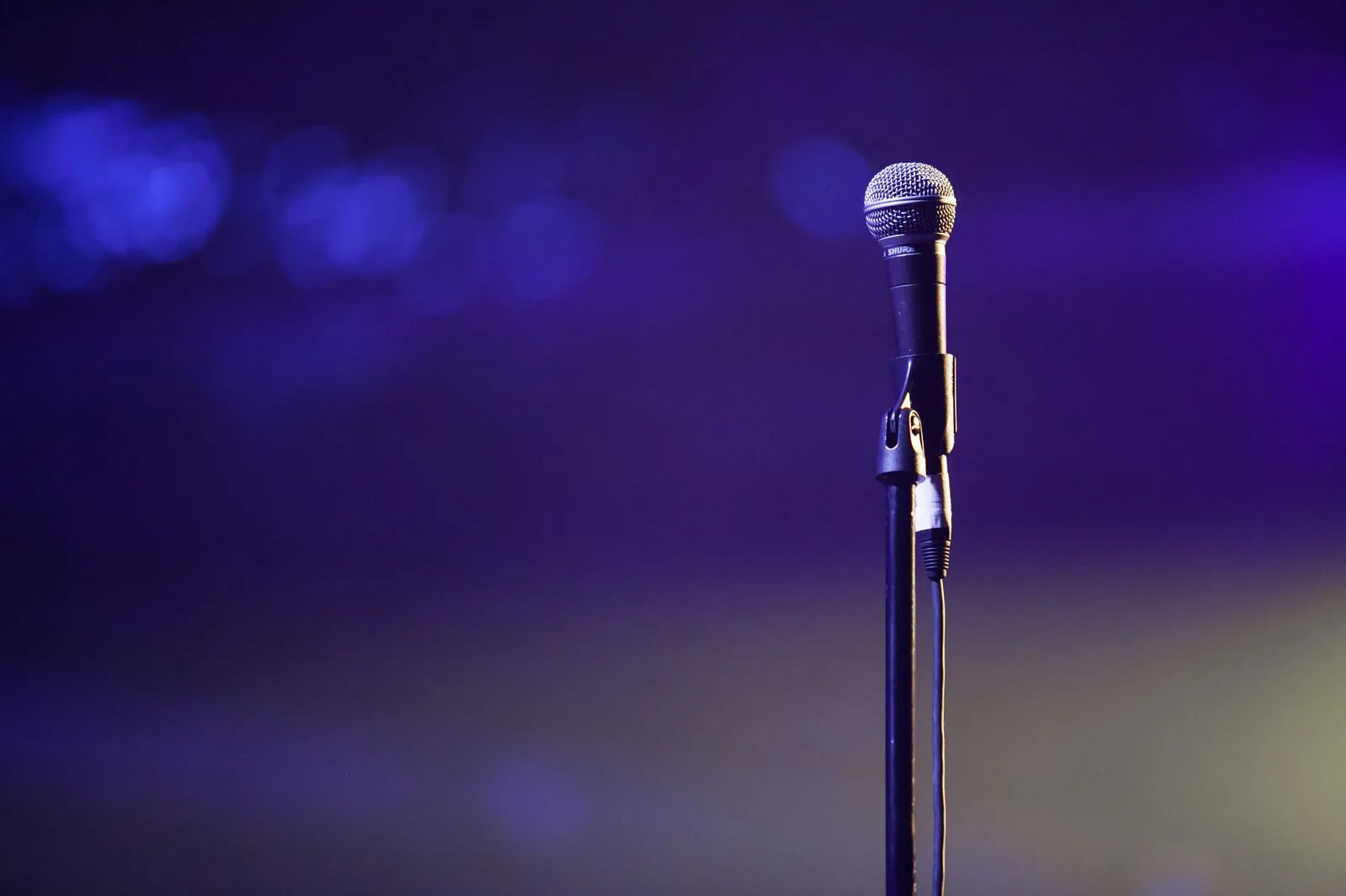 Microfone num pedestal contra fundo roxo desfocado, foto de banco de imagens sem relação com os comediantes