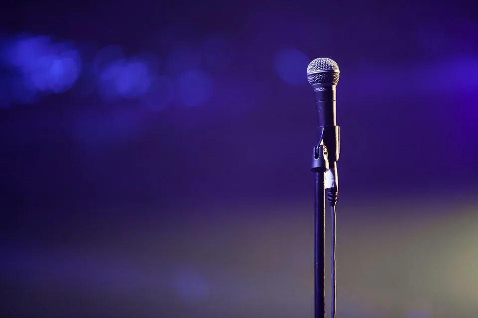 Microfone num pedestal contra fundo roxo desfocado, foto de banco de imagens sem relação com os comediantes