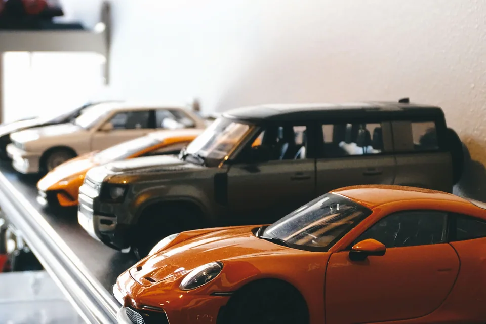 Miniaturas de carros alinhadas em prateleira, com um Porsche laranja em primeiro plano