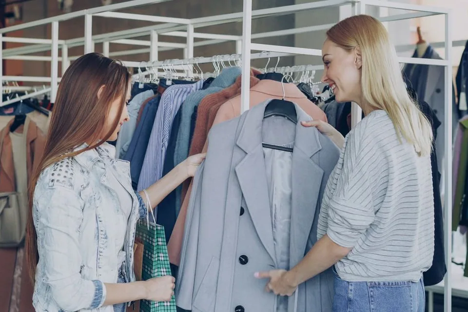 Duas mulheres olhando um blazer cinza em arara de loja de roupas