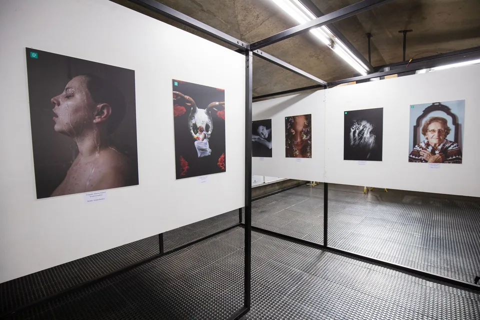 Paredes brancas de uma sala expositiva com fotografias emolduradas e etiquetas de identificação