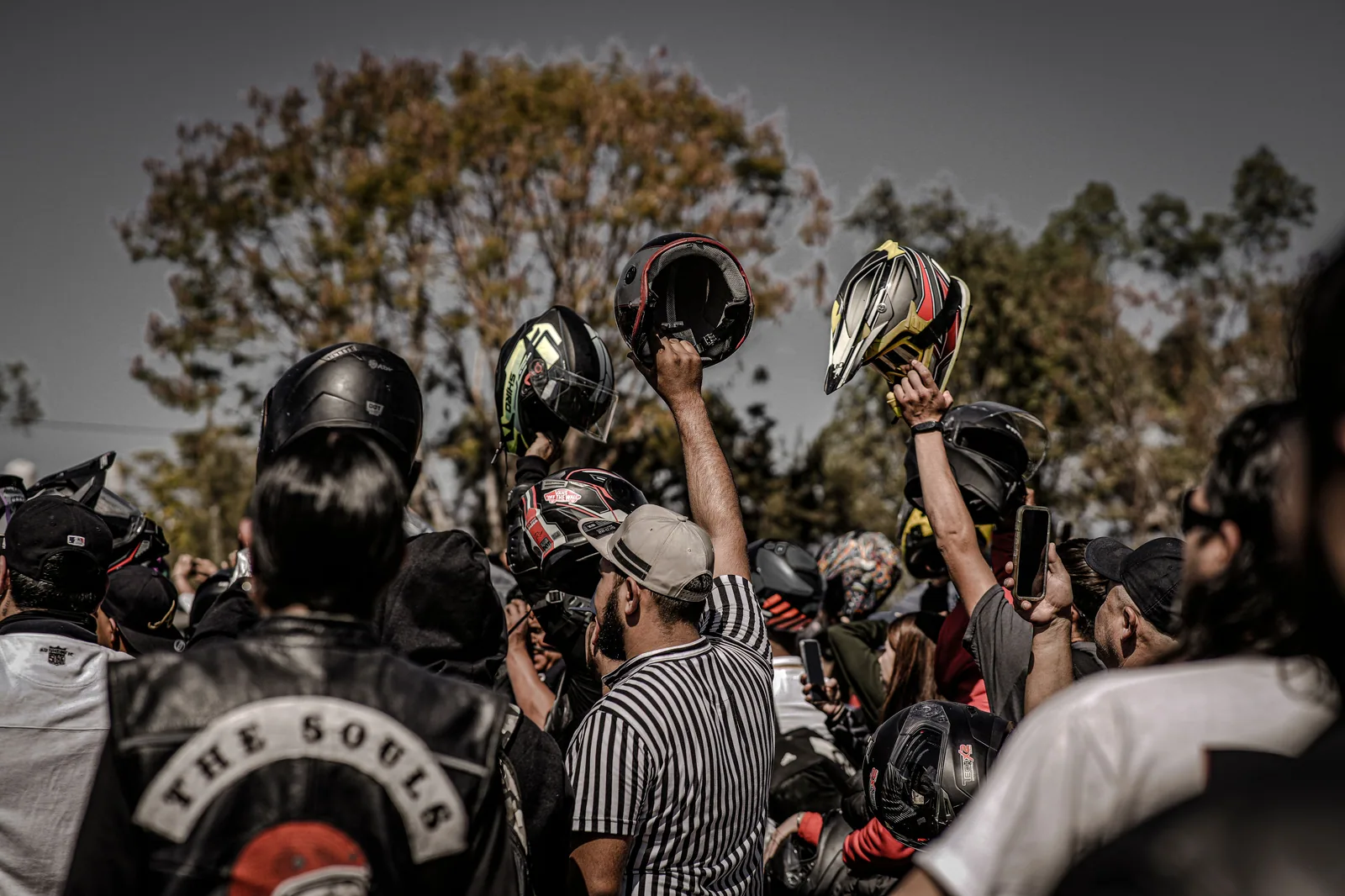 Motociclistas reunidos ao ar livre erguem capacetes durante encontro de motoclubes