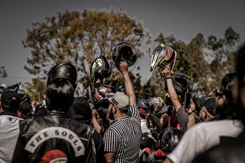 Motociclistas reunidos ao ar livre erguem capacetes durante encontro de motoclubes