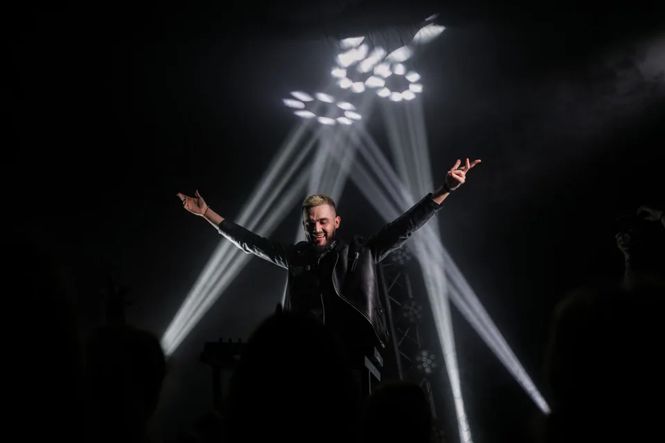 Artista no palco com os braços abertos, sob feixes de luz