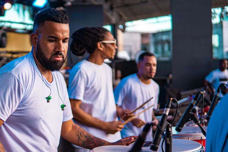 Naipe de percussao de um grupo de pagode tocando surdo e repique em palco, com microfones na frente dos tambores