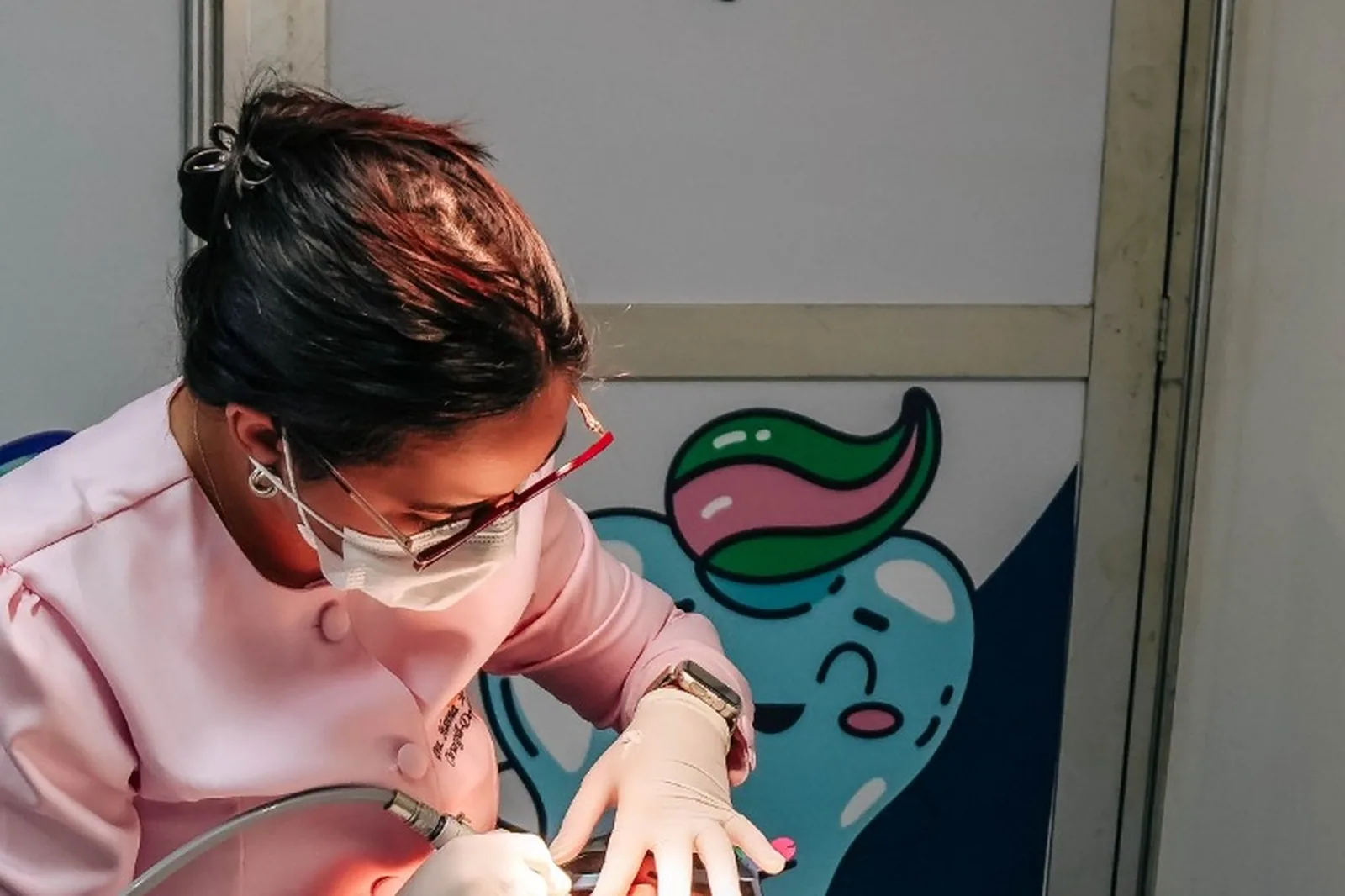 Dentista de jaleco rosa e óculos atende paciente diante do mascote em forma de dente no Odonto em Ação