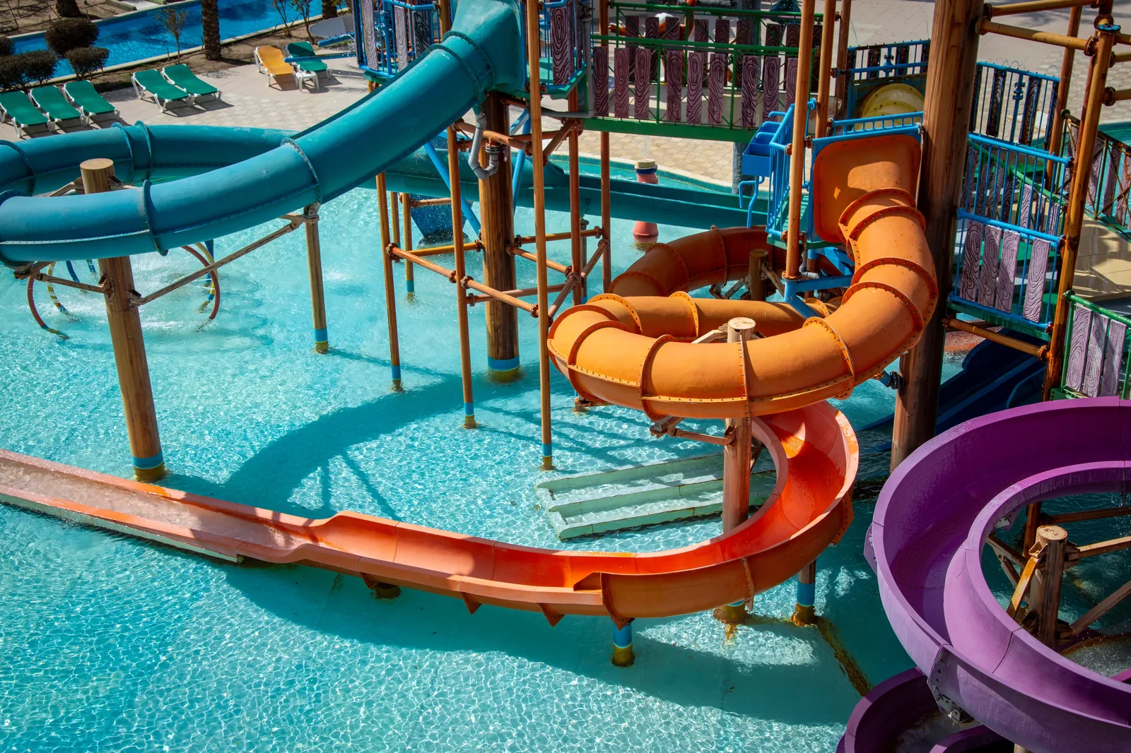 Toboáguas laranja, verde-água e roxo sobre piscina de parque aquático, vistos de cima
