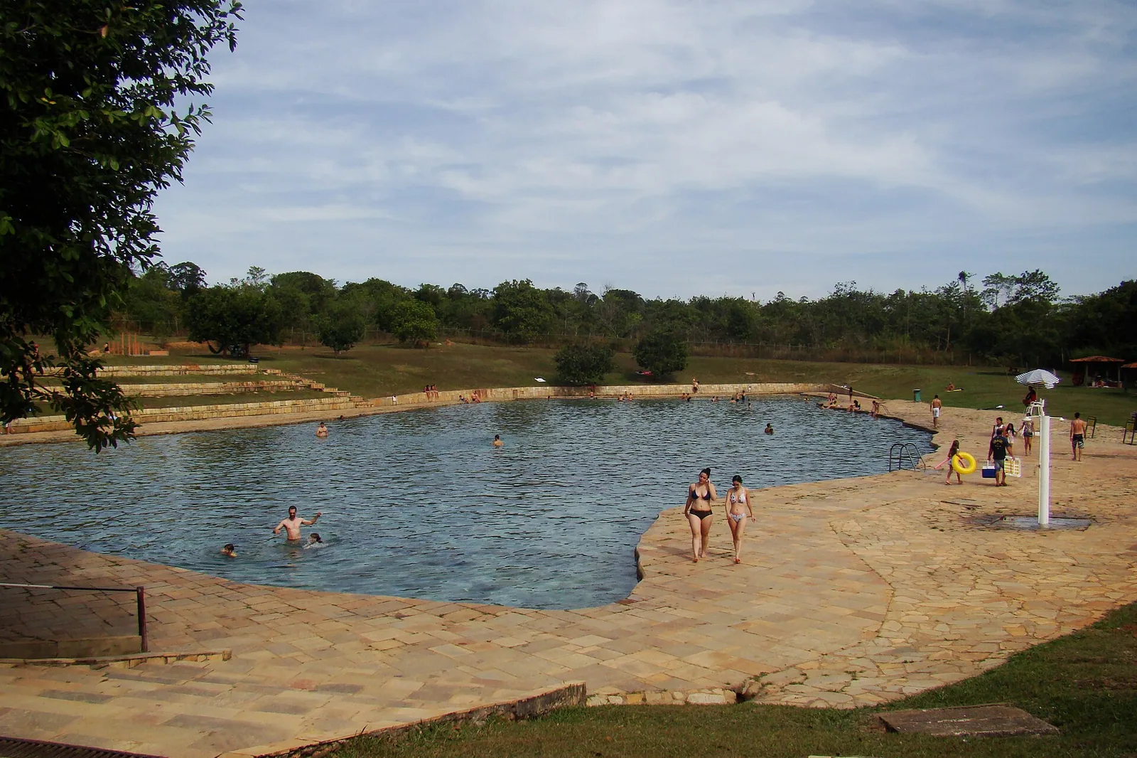 Vista ampla da piscina Pedreira, no Parque Nacional de Brasília, com pessoas na água e piso de pedra ao redor