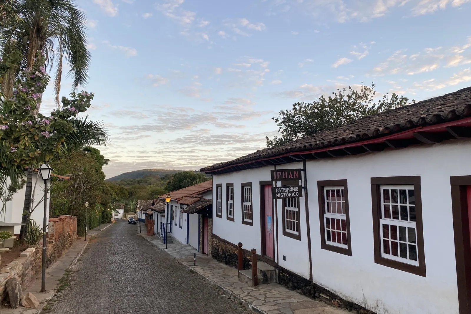 Rua de pedras com casarões brancos de janelas de madeira no Centro Histórico de Pirenópolis, ao entardecer.