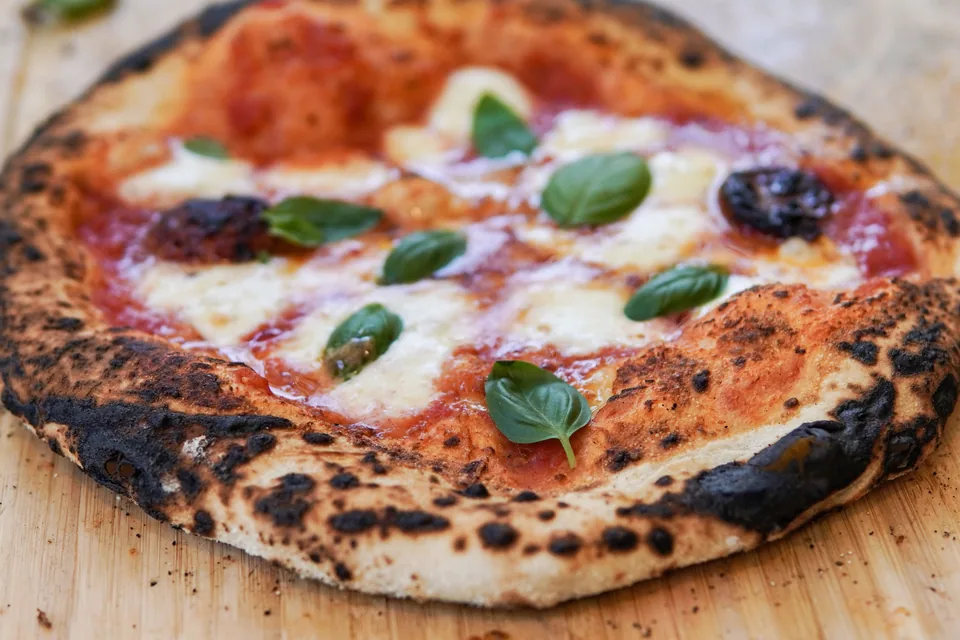 Pizza margherita de borda queimada em tábua de madeira, em foto ilustrativa