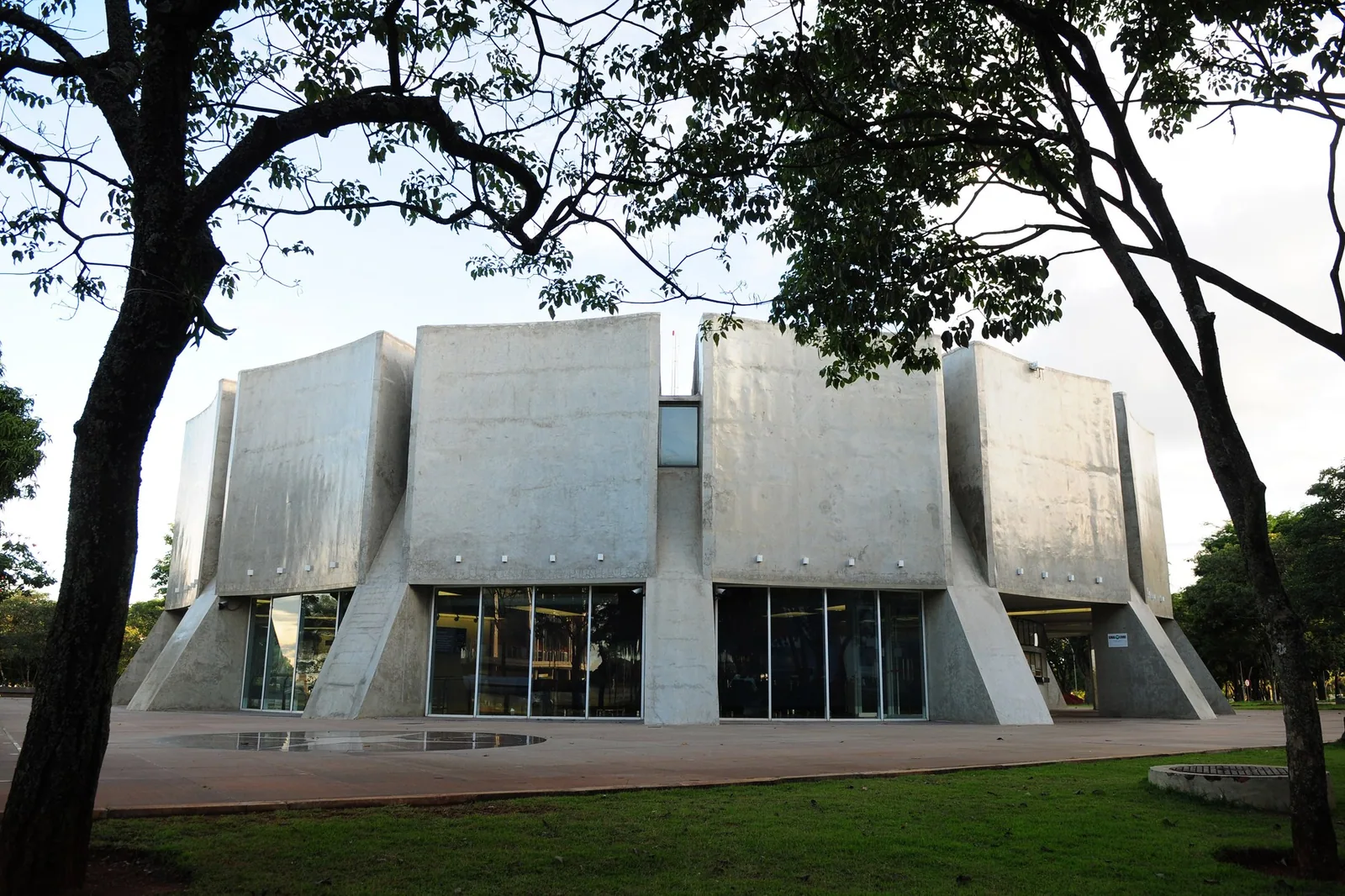 Fachada de concreto do Planetário de Brasília, entre árvores, na luz do fim de tarde