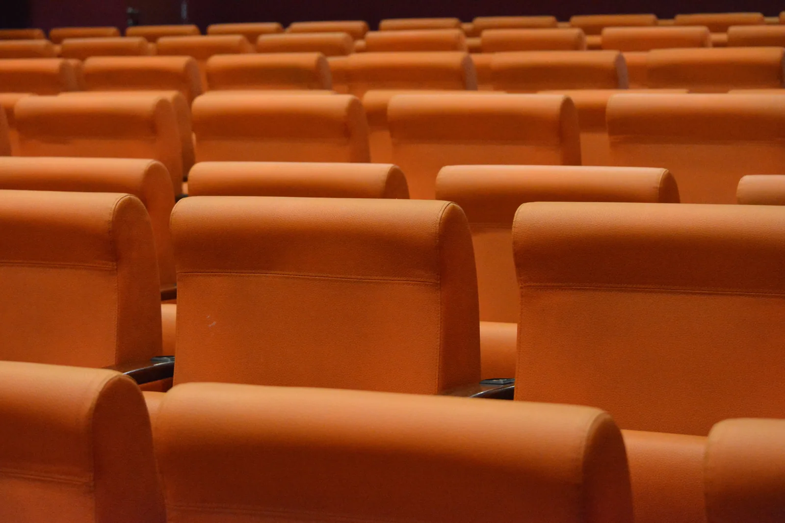 Fileiras de poltronas laranjas vazias em um teatro, vistas de perto.