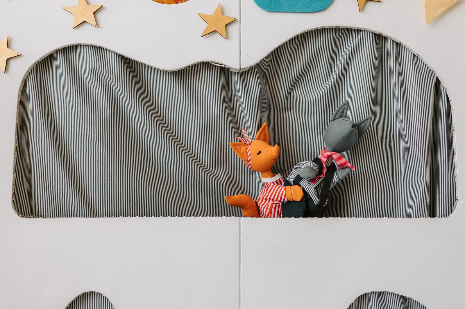 Dois fantoches de pano, uma raposa laranja e um lobo cinza, em um palquinho de teatro infantil (foto ilustrativa, não é da montagem)
