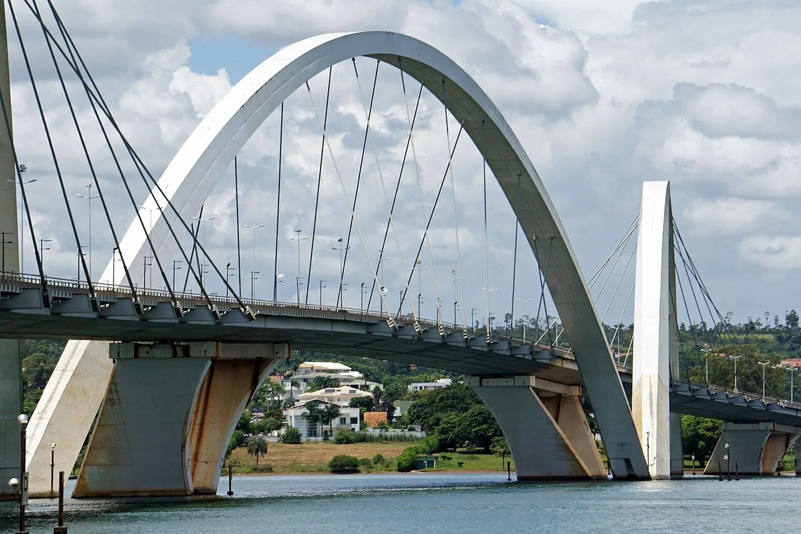 Arco central da Ponte JK visto da água do Lago Paranoá, com casas do Lago Sul ao fundo