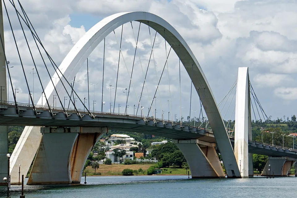 Arco central da Ponte JK visto da água do Lago Paranoá, com casas do Lago Sul ao fundo