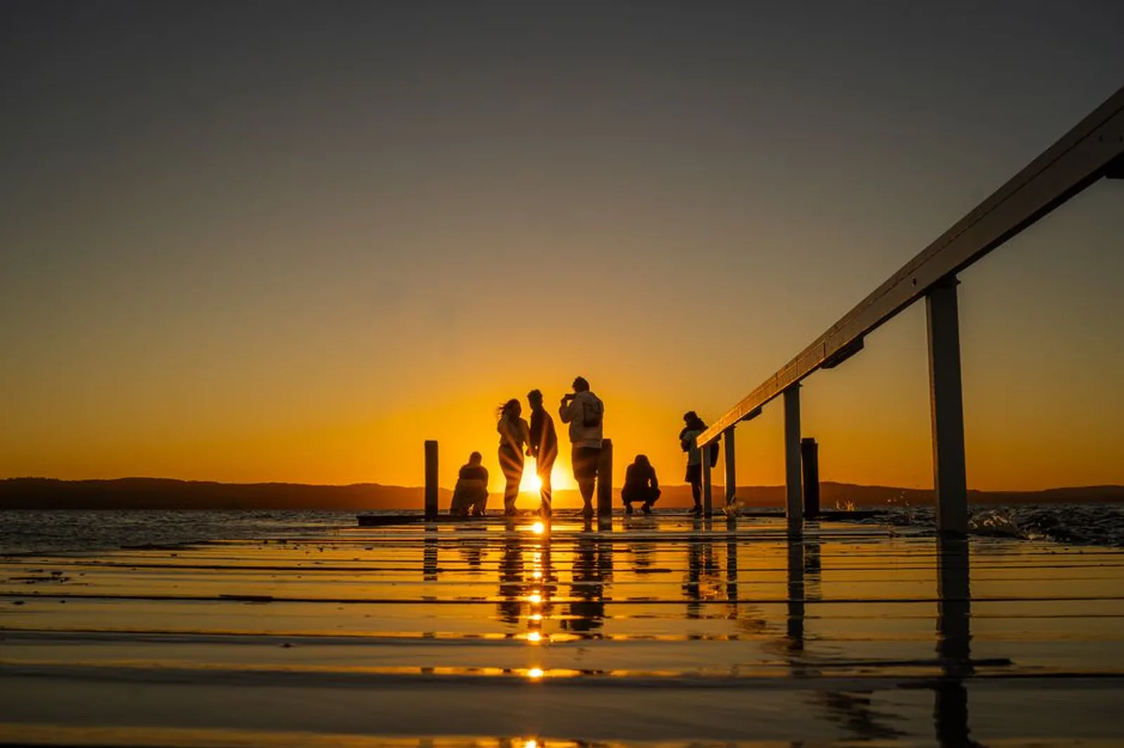 Silhuetas de pessoas em um deck observando o pôr do sol sobre a água