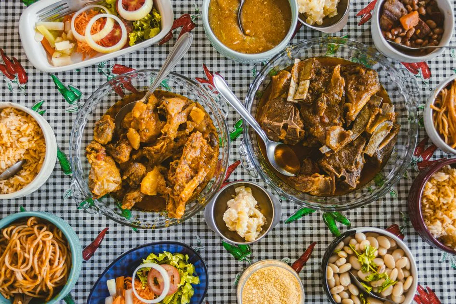 Mesa com travessas de carnes, arroz, feijão, farofa e saladas, sobre toalha xadrez (foto ilustrativa, não é da Quituart)