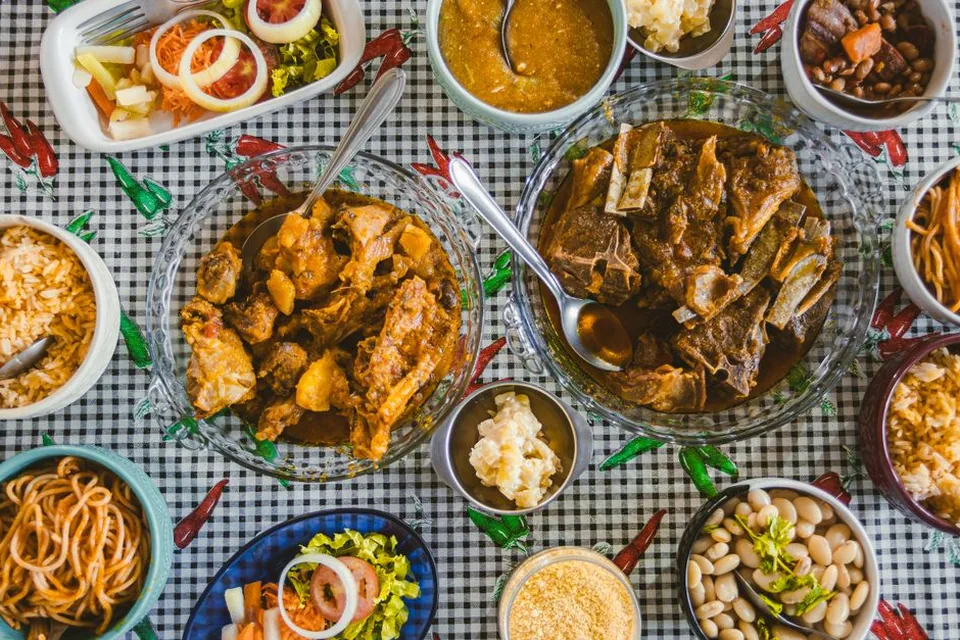 Mesa com travessas de carnes, arroz, feijão, farofa e saladas, sobre toalha xadrez (foto ilustrativa, não é da Quituart)