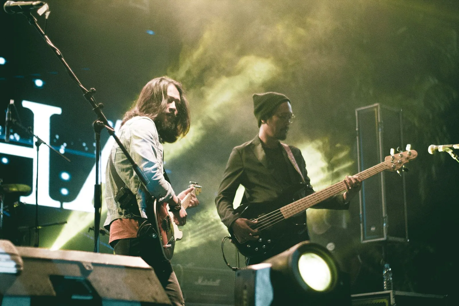 Guitarrista e baixista tocando em um palco com fumaça e luz amarela