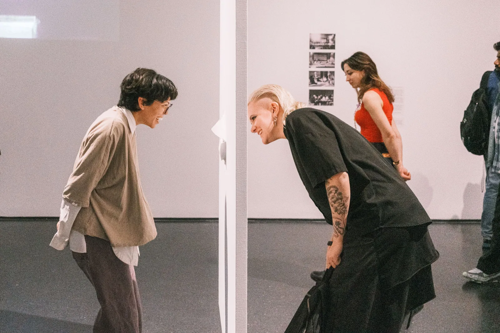 Duas pessoas curvadas frente a frente diante de uma instalação em uma sala de exposição