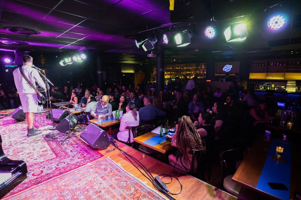 Banda tocando ao vivo em uma casa de shows com plateia sentada às mesas