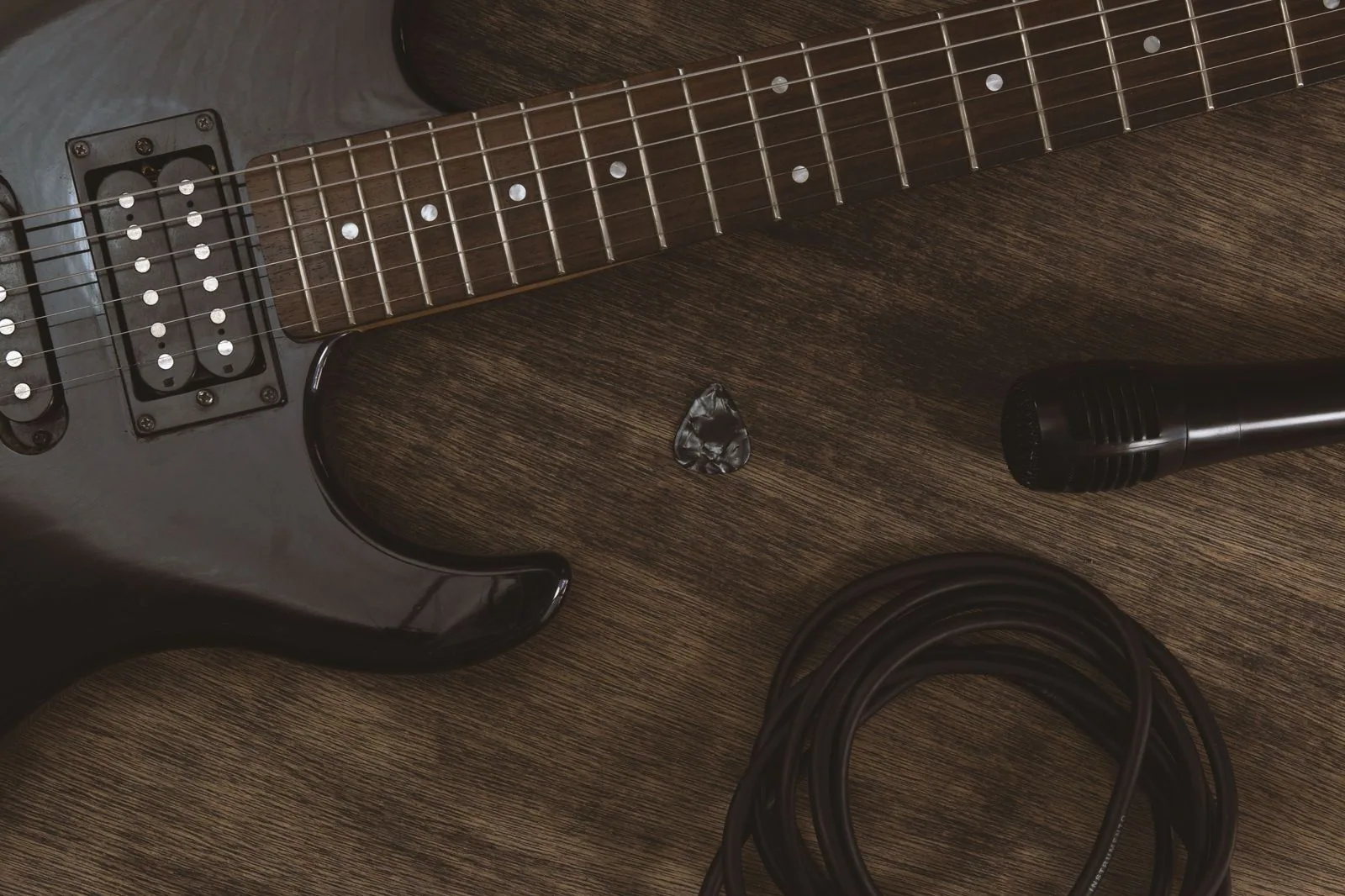 Guitarra elétrica, microfone, palheta e cabo sobre mesa de madeira (foto ilustrativa)