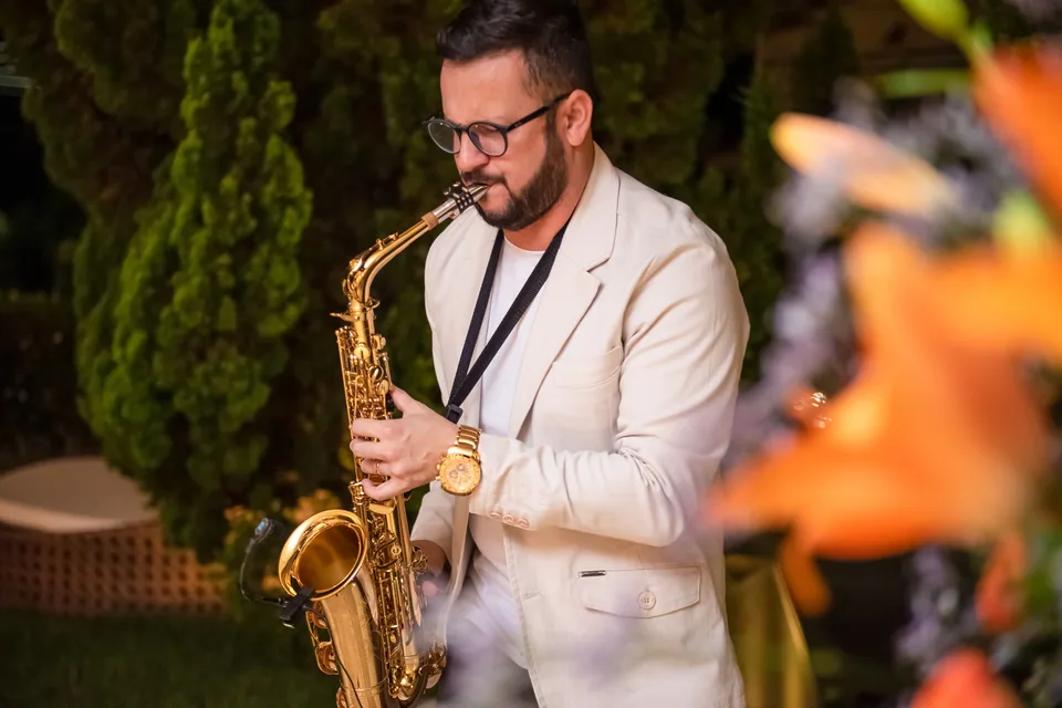 Saxofonista de terno claro tocando ao ar livre em área de jardim, à noite