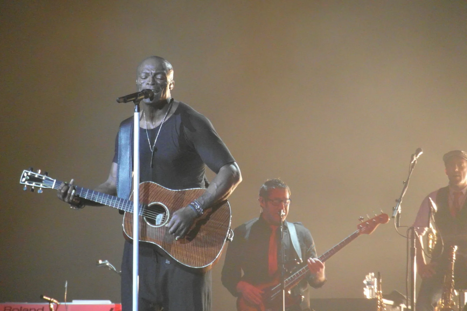 Seal cantando e tocando violão em um palco, com baixista e saxofonista ao fundo, em foto de arquivo de 2012