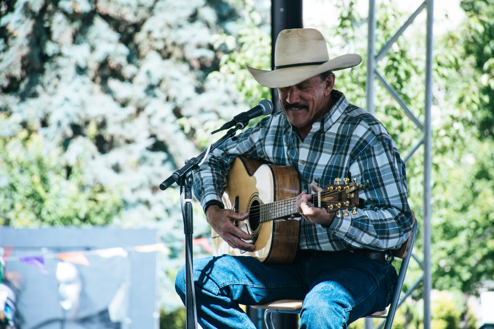 Músico de chapéu de cowboy toca violão em palco ao ar livre