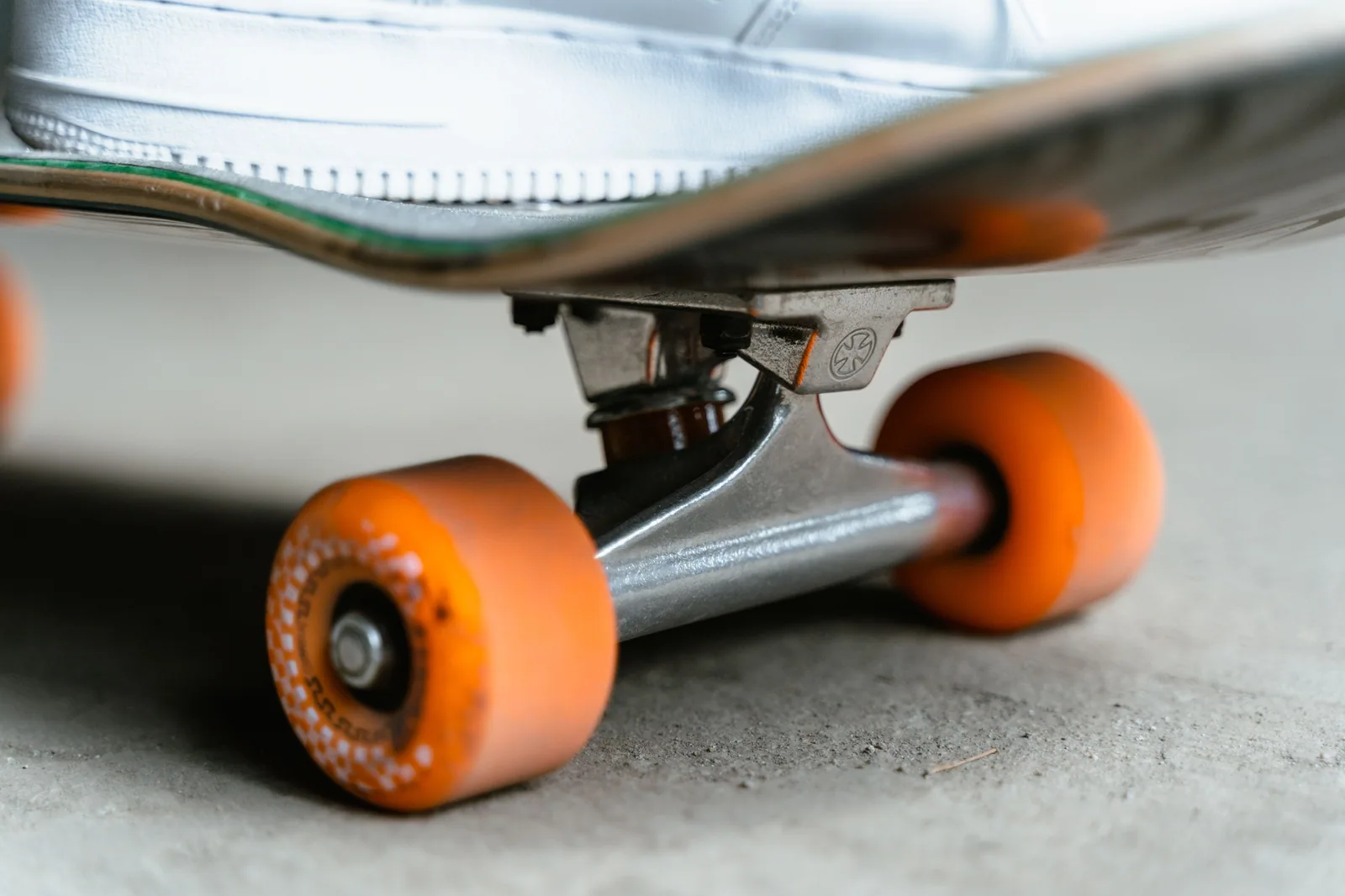 Detalhe de um skate visto de baixo, com rodas laranjas e truck de metal sobre o concreto
