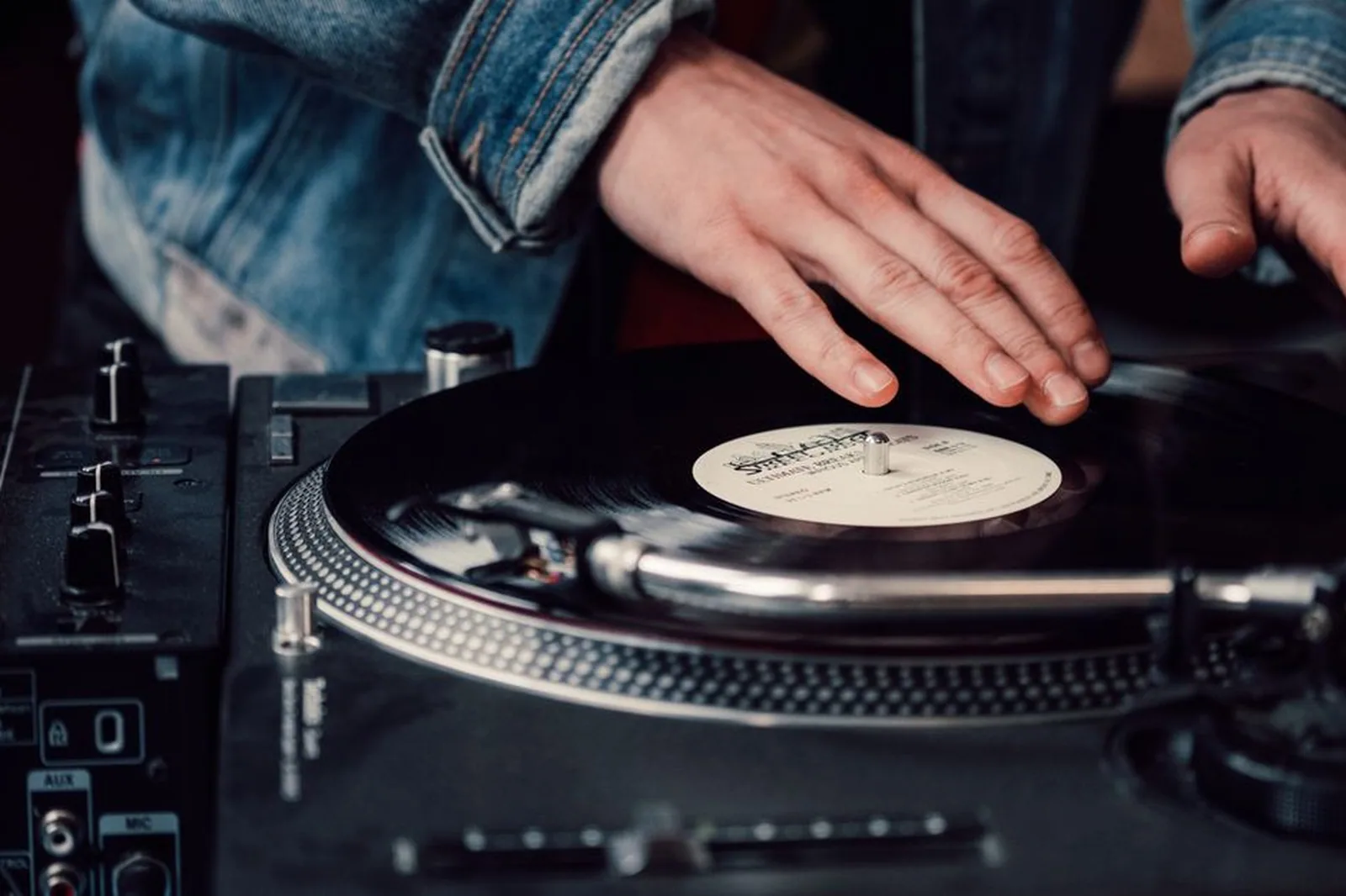 Mãos de um DJ sobre um disco de vinil em uma mesa de som (foto ilustrativa, não é da Lobby)