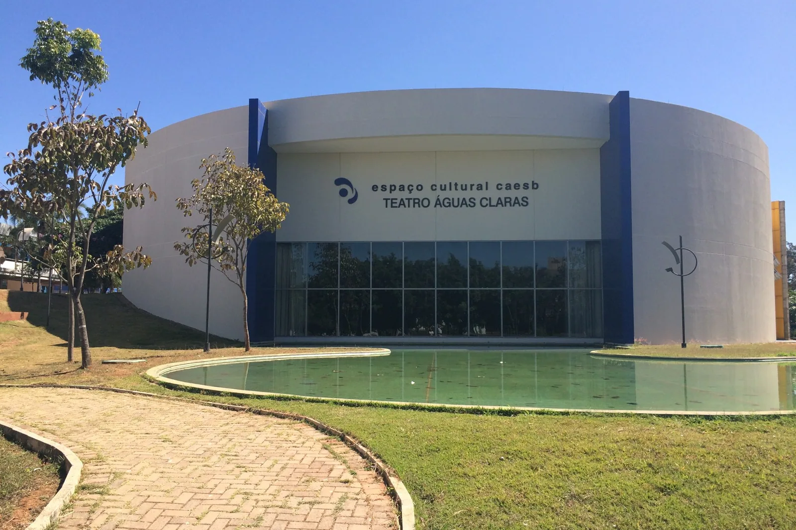 Fachada circular do Espaço Cultural Caesb, onde funciona o Teatro Águas Claras, com espelho d'água e gramado na frente