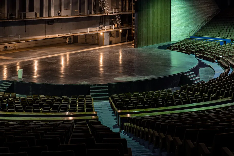 Palco de teatro vazio com poltronas em curva e iluminação verde