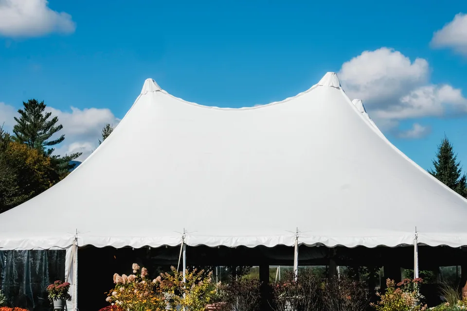 Tenda branca de evento montada ao ar livre, vista de baixo, com o céu azul ao fundo