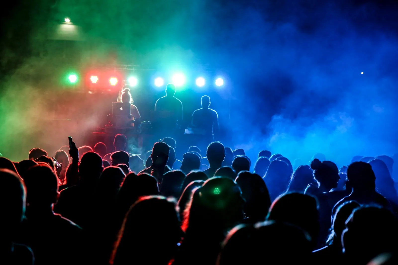 Silhuetas de DJs em palco com luzes verdes, vermelhas e azuis diante de uma pista cheia