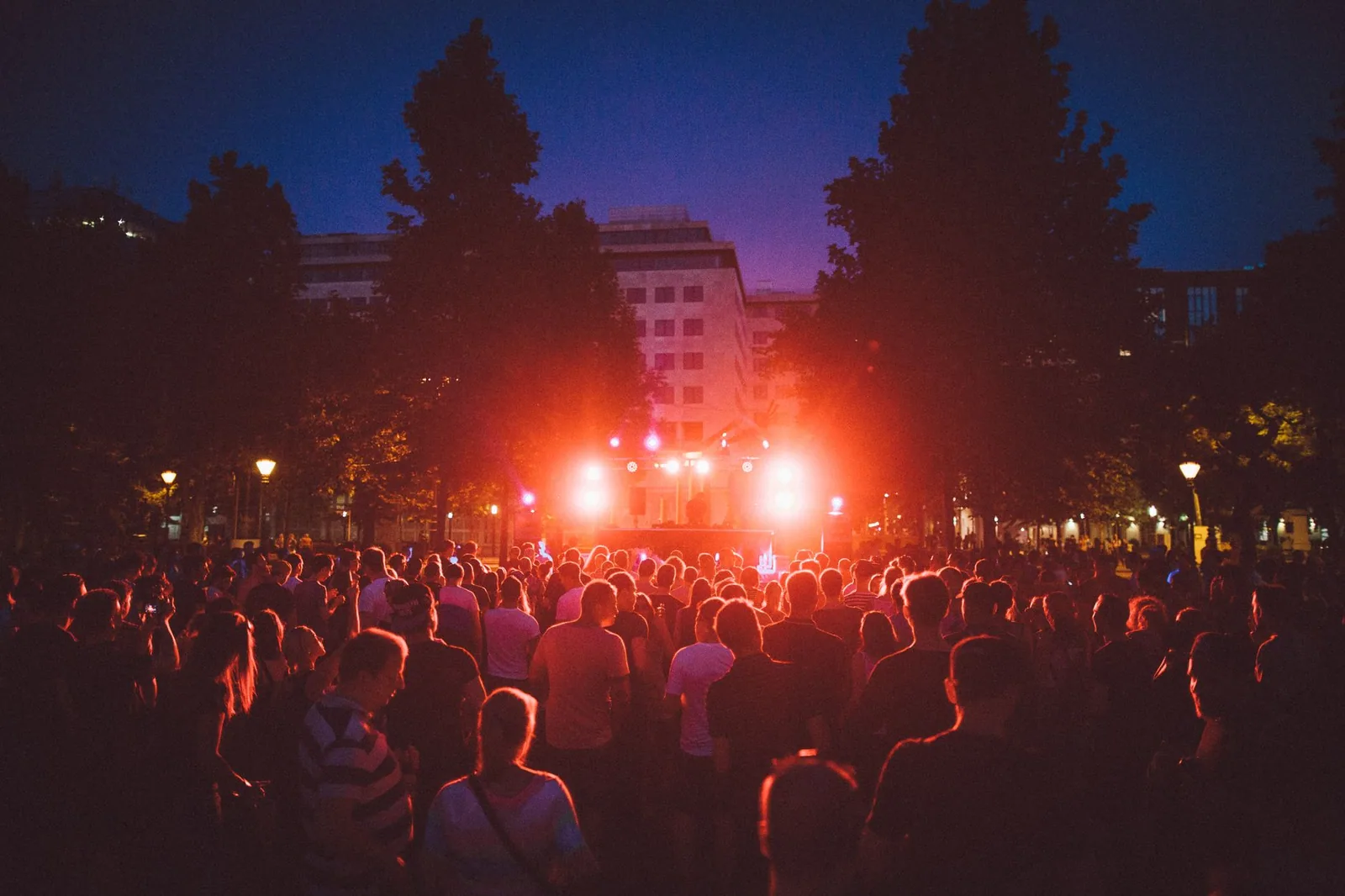 Multidão em frente a um palco com luzes vermelhas ao anoitecer, em festa de música eletrônica ao ar livre