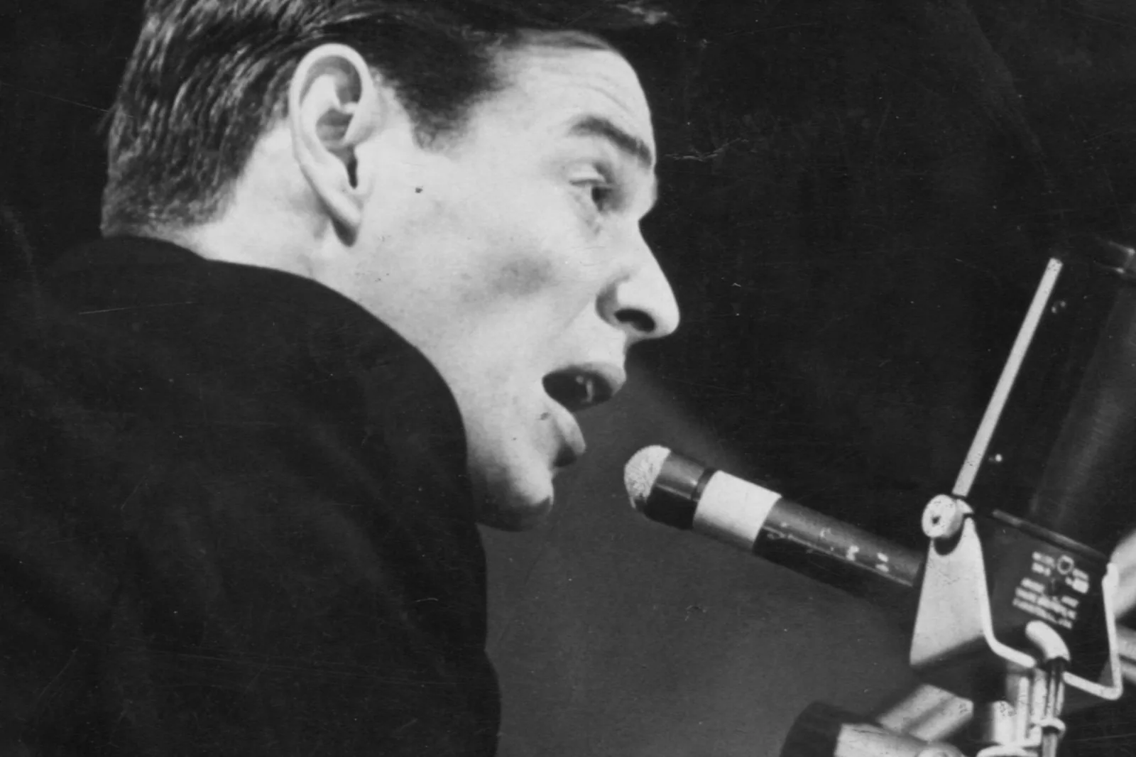 Retrato em preto e branco de Tom Jobim cantando diante de um microfone, em 1965