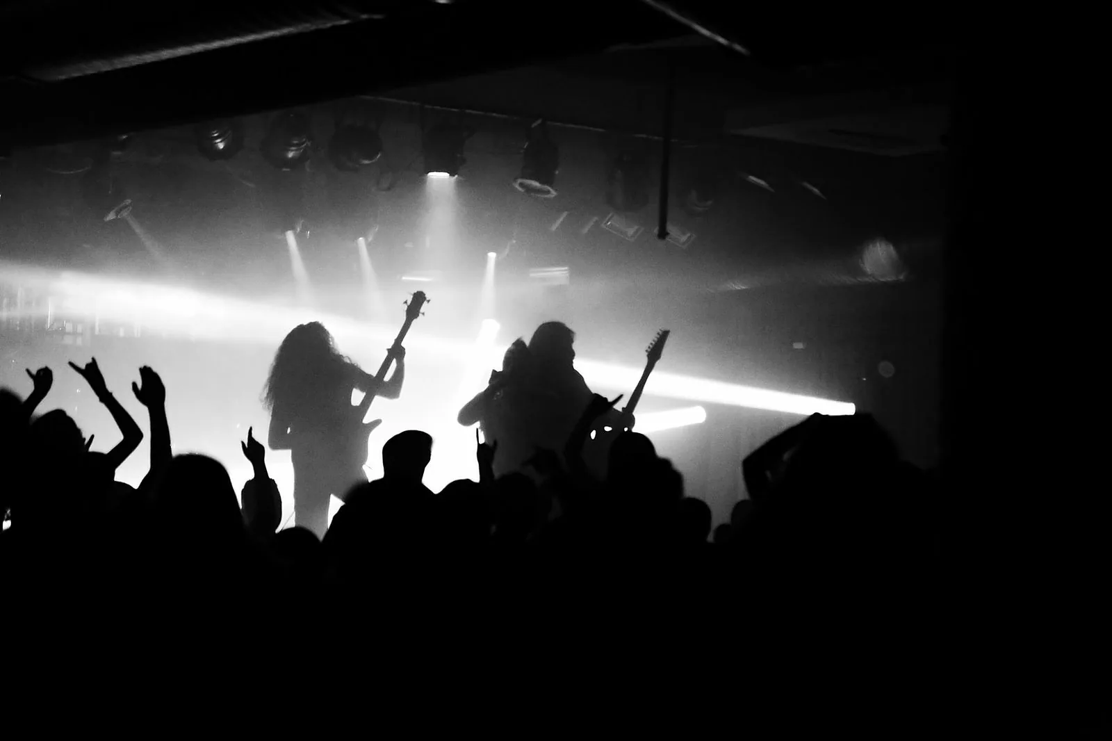Silhueta de banda de rock no palco diante do público de braços erguidos, em preto e branco