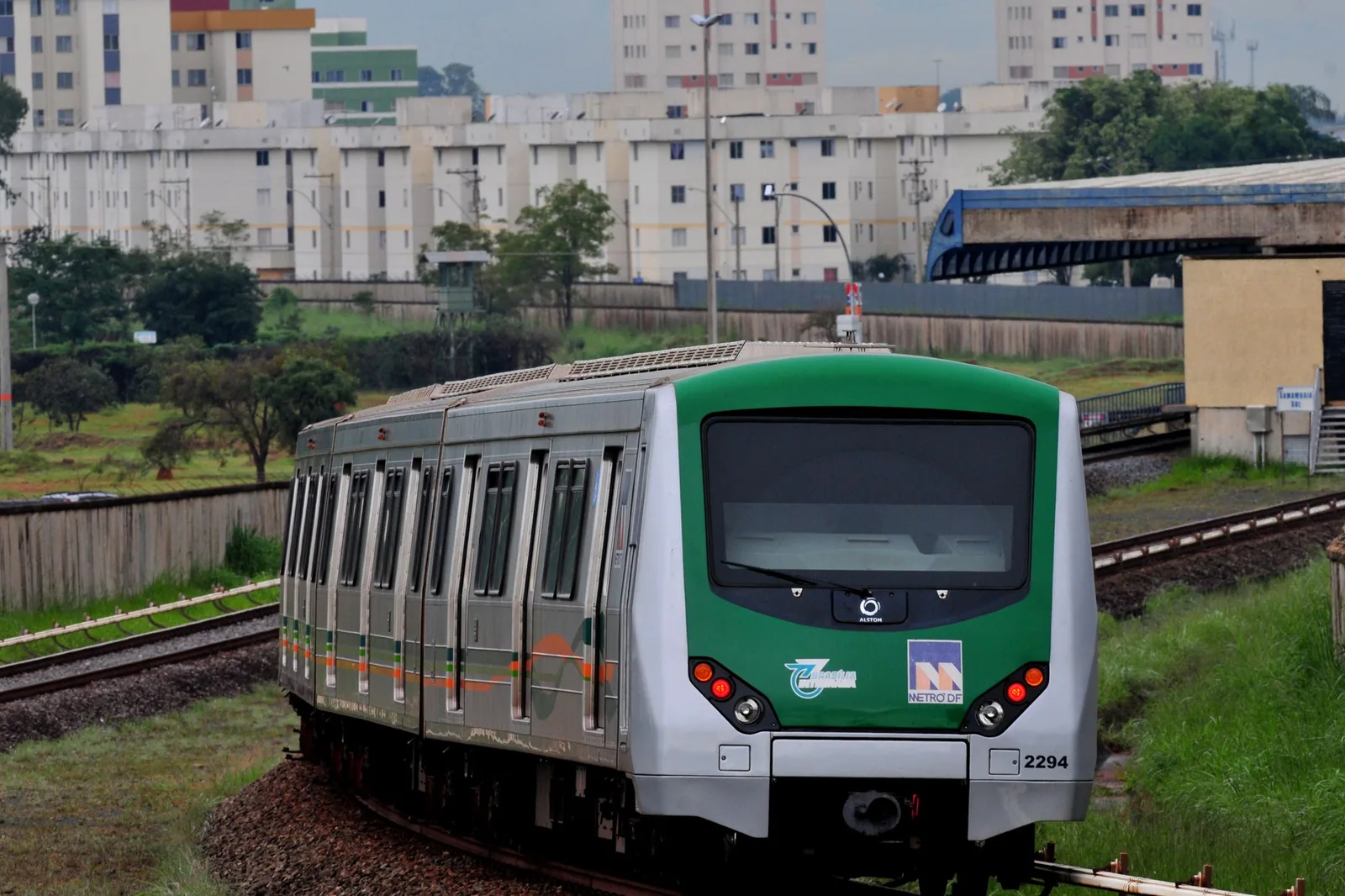 Trem verde e prata do Metrô-DF em curva, com blocos de apartamentos ao fundo (foto de arquivo)