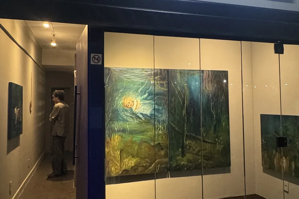 Fachada do deCurators à noite com pinturas da exposição Trieb+ expostas na vitrine